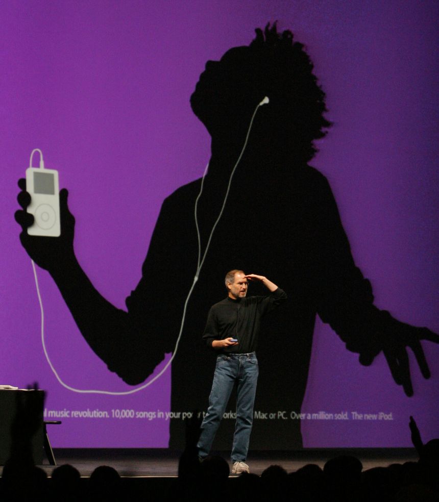 Apple CEO Steve Jobs looks out over the crowd as a new television commercial for Apple iPod digital music is displayed behind him, at the 2004 Macworld Conference and Expo in San Francisco, January 6, 2004.