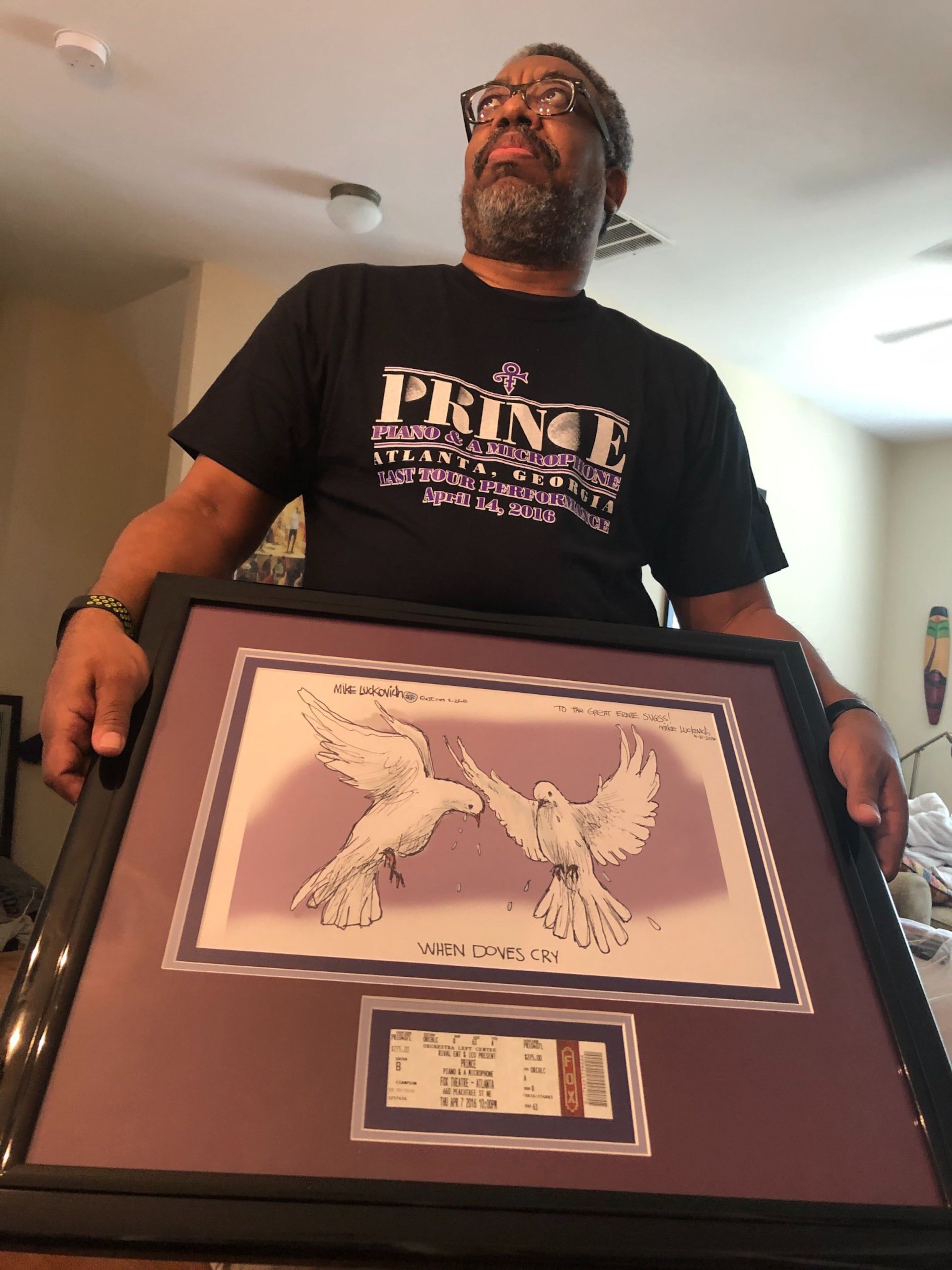 AJC Reporter Ernie Suggs holding an original piece by AJC cartoonist Mike Luckovich that was drawn as an editorial cartoon the day Prince died. (Ernie Suggs/AJC)