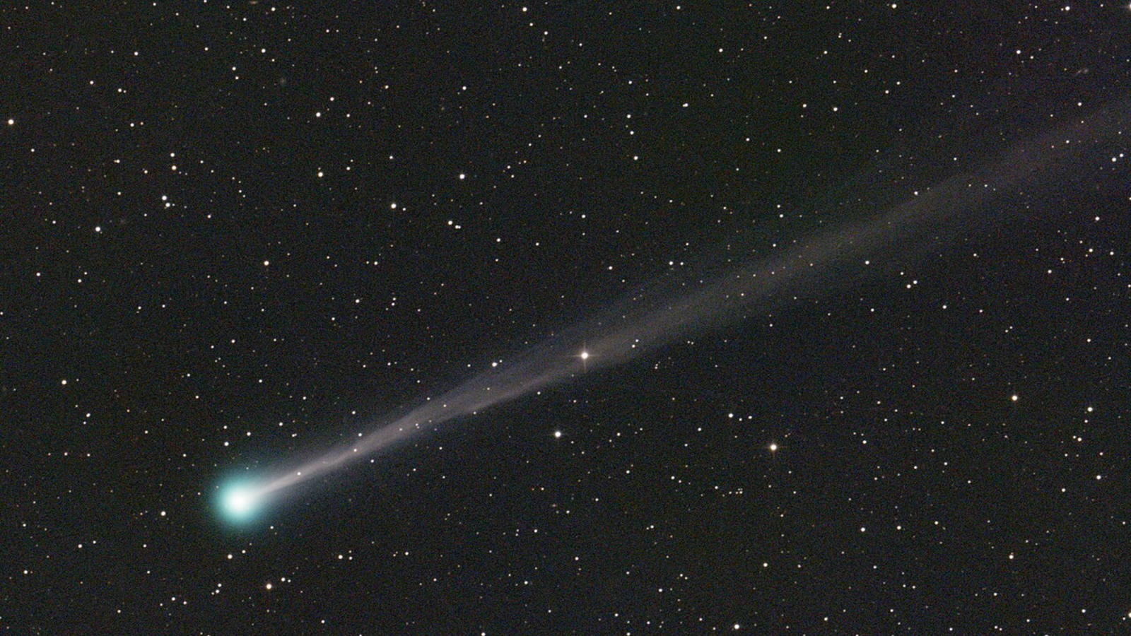 An astronomical photo of a comet and its long tail with the starry backdrop of space