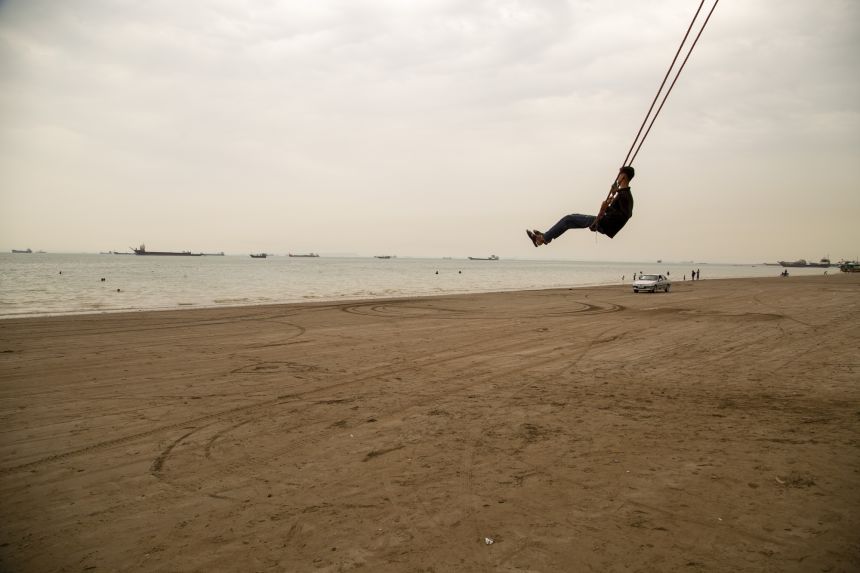 A man swings from a giant rope swing on the beach as ships are anchored near the shoreline on April 22, 2026 in Bandar Abbas, Iran. Bandar Abbas is a port city and the capital of Hormozgan Province, along the Persian Gulf and Strait of Hormuz.